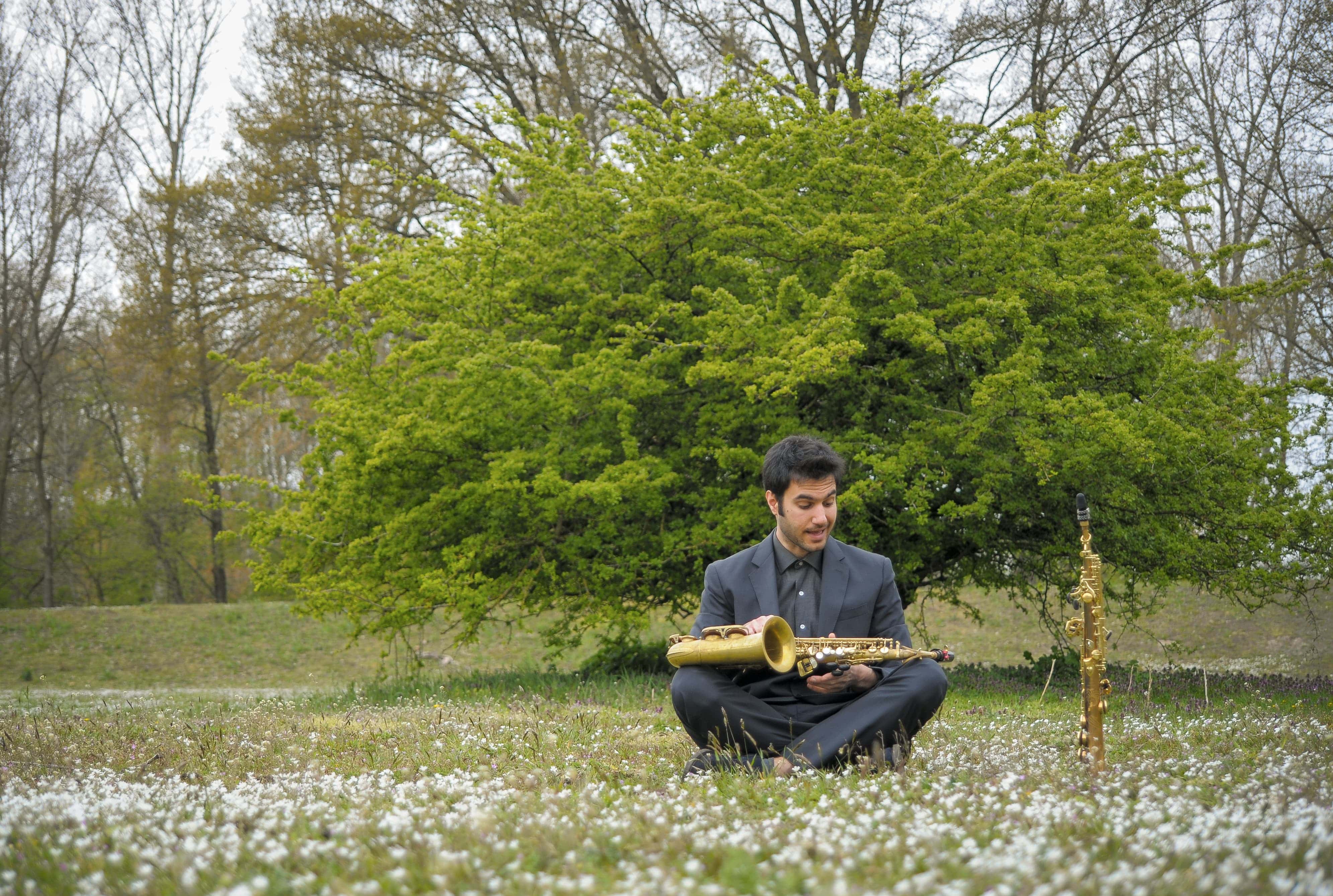 the artist sitting on the grass with his saxophone